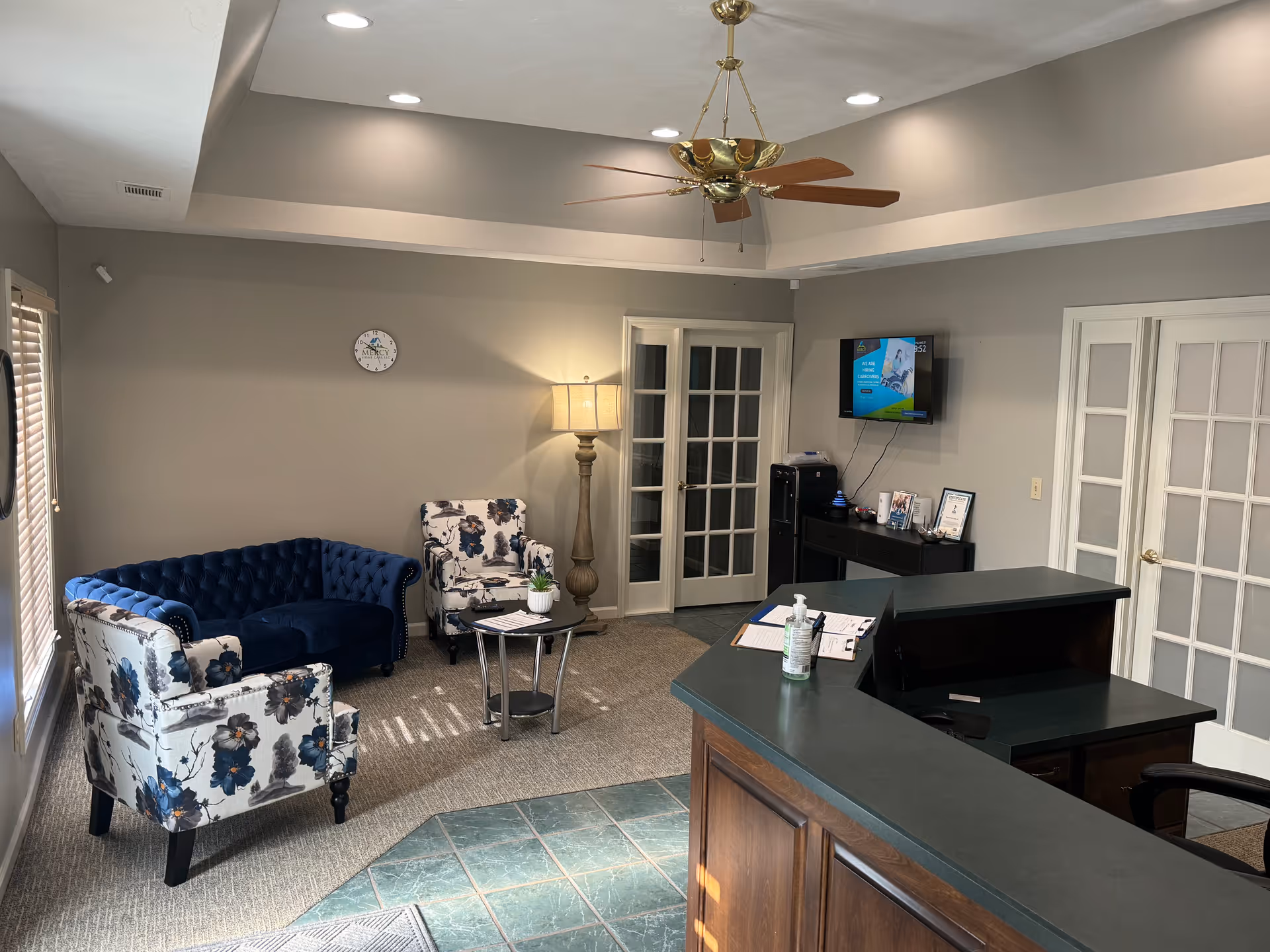 Reception area with curved dark desk, seating, TV, and glass doors in a quiet lobby.