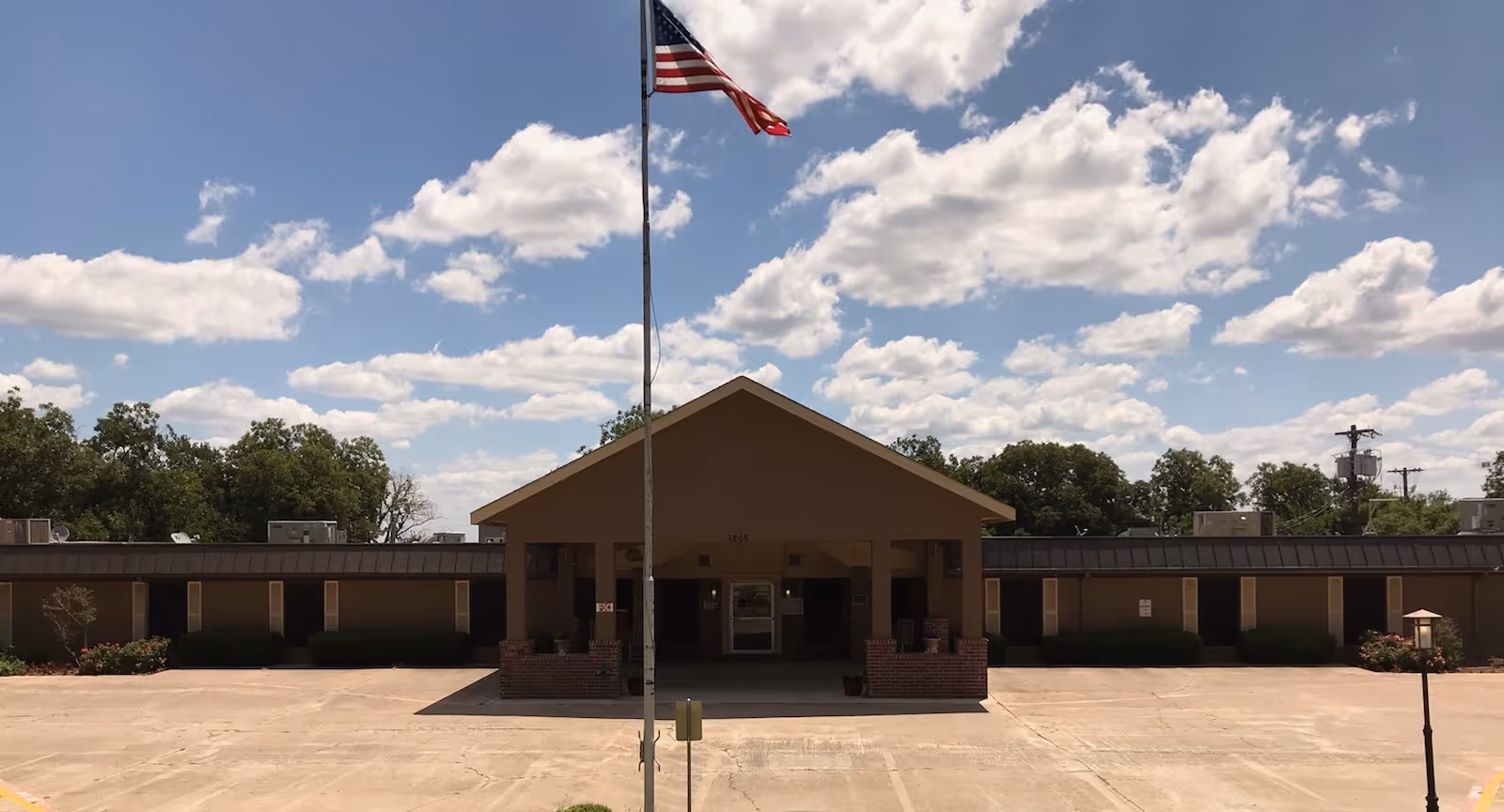 Resthome exterior: single-story building with peaked entrance, flagpole, and empty parking lot.