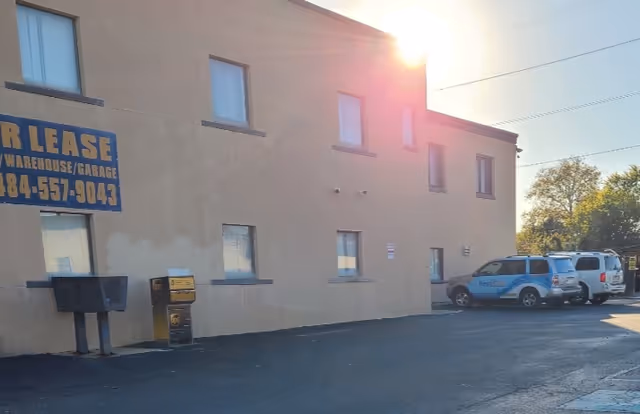 Beige building exterior with a FOR LEASE sign and two blue vans parked nearby.