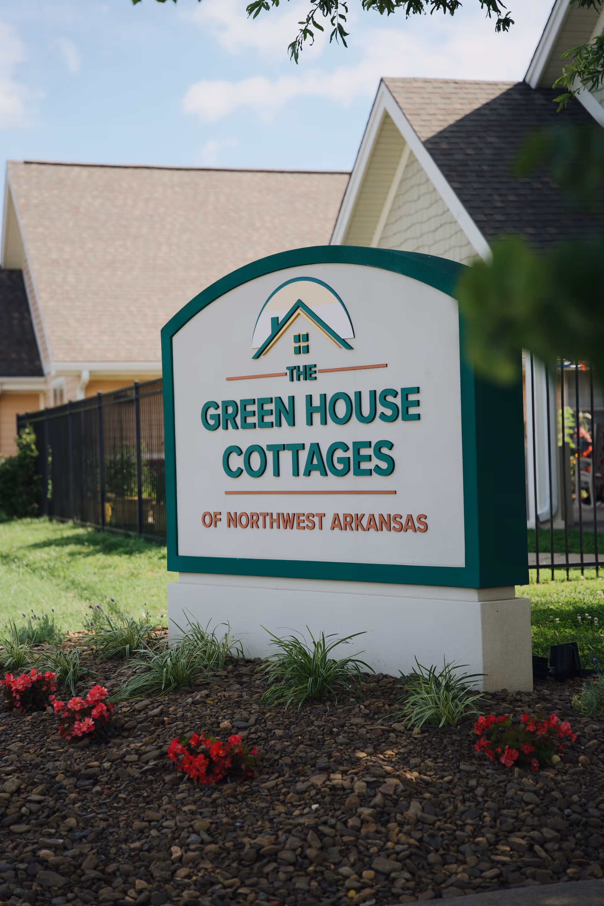 Outdoor sign reads The Green House Cottages in front of a building with landscaping.