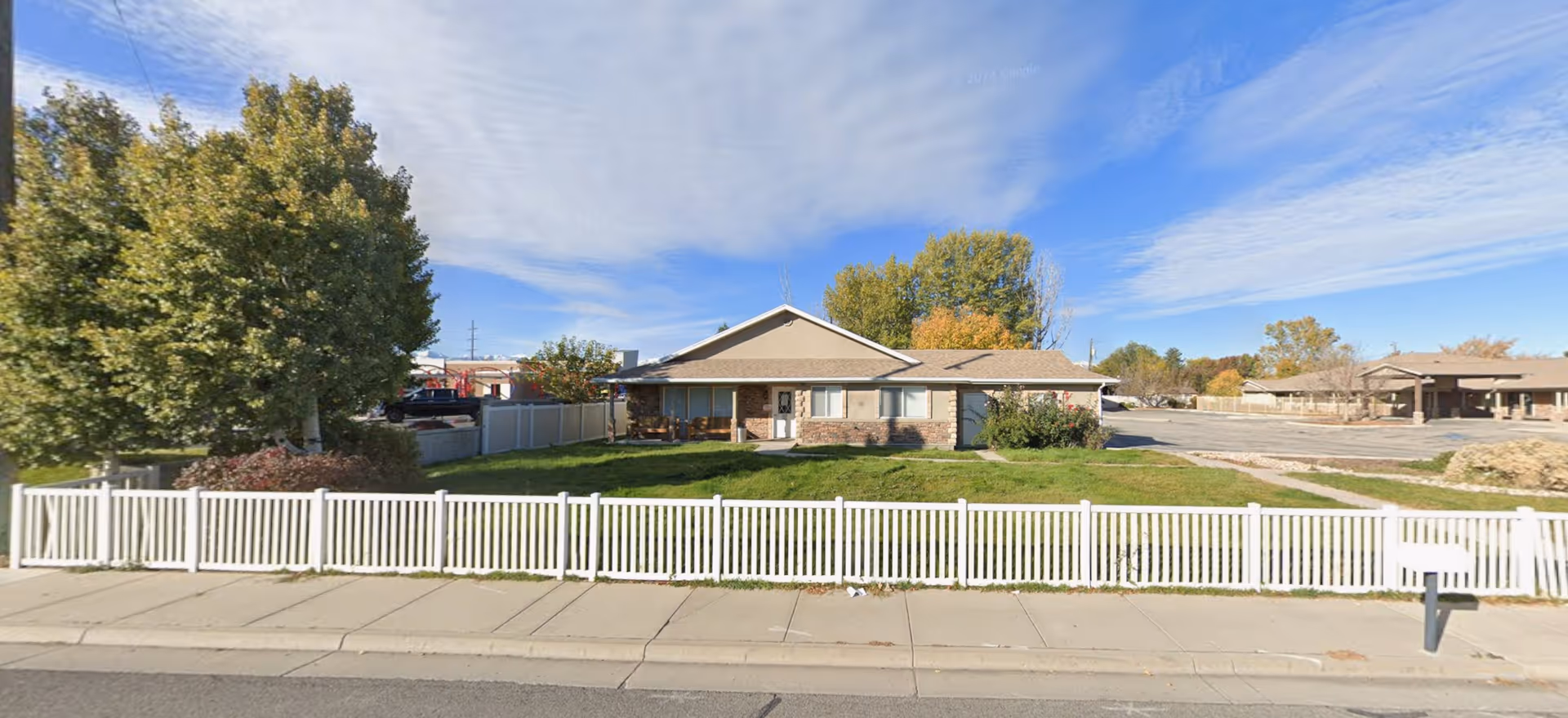 Single story beige building behind a white picket fence with a green lawn.
