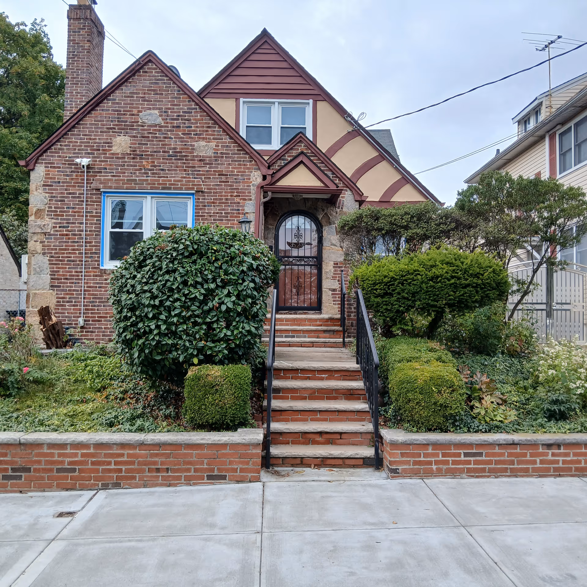 Brick house front with arched door, steps, and landscaped garden.