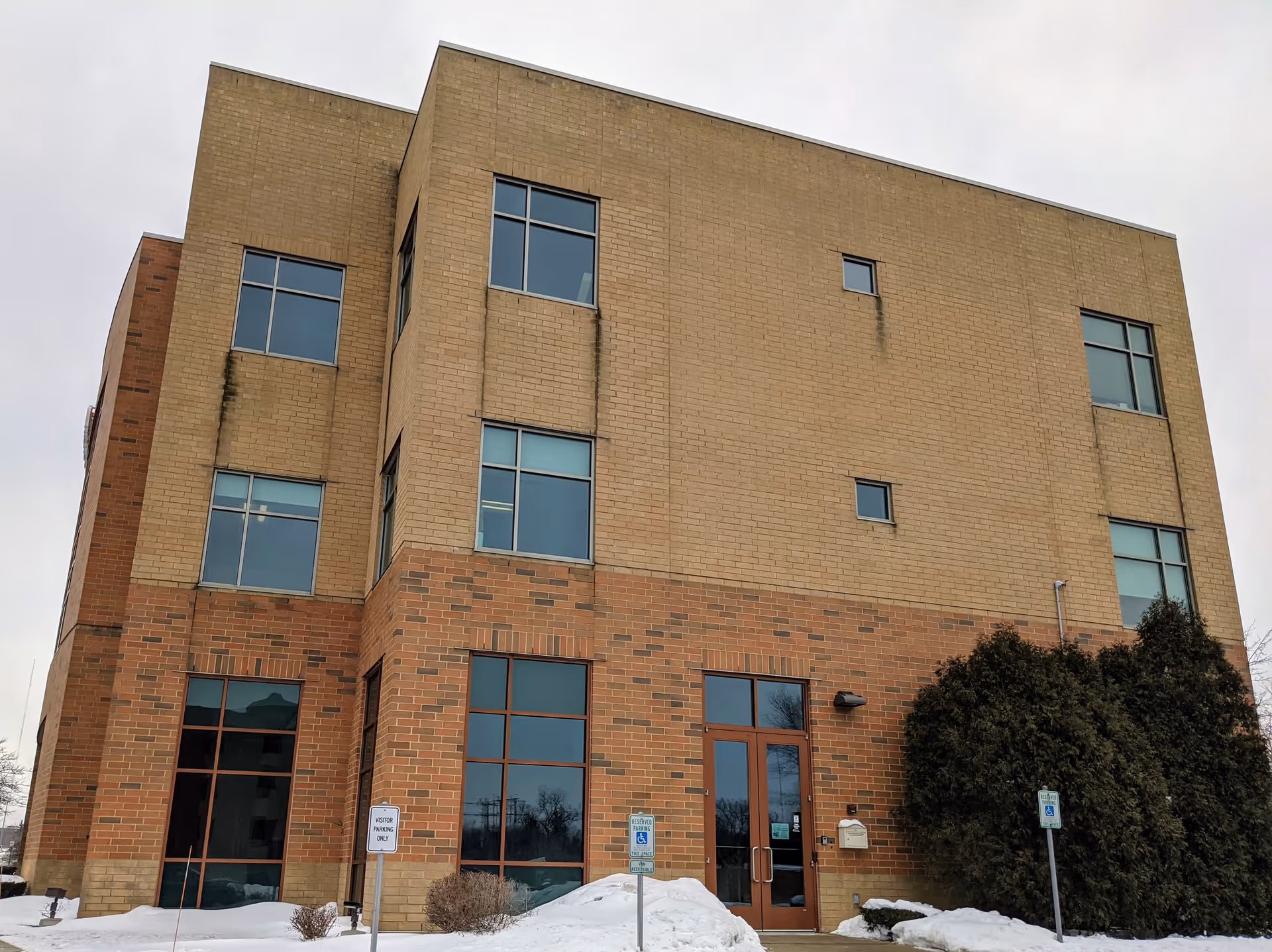 Three-story brick building with beige upper and red lower facade and glass entry.