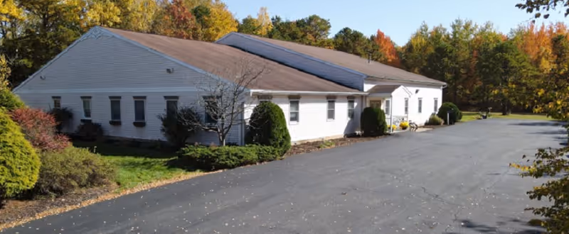 Exterior view of The Corrigan House: a long white building with a driveway and fall trees.