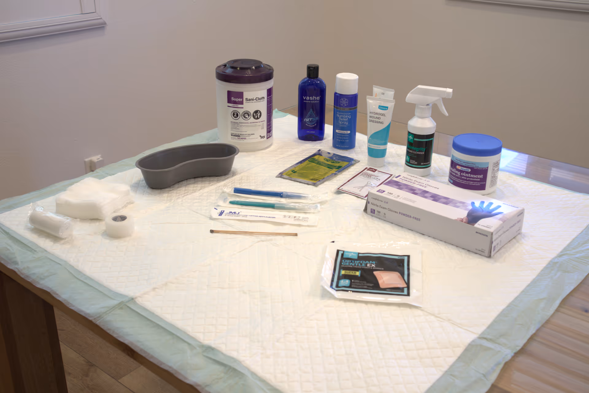Table laid with wound care supplies including dressings, bottles, and a gray kidney dish.