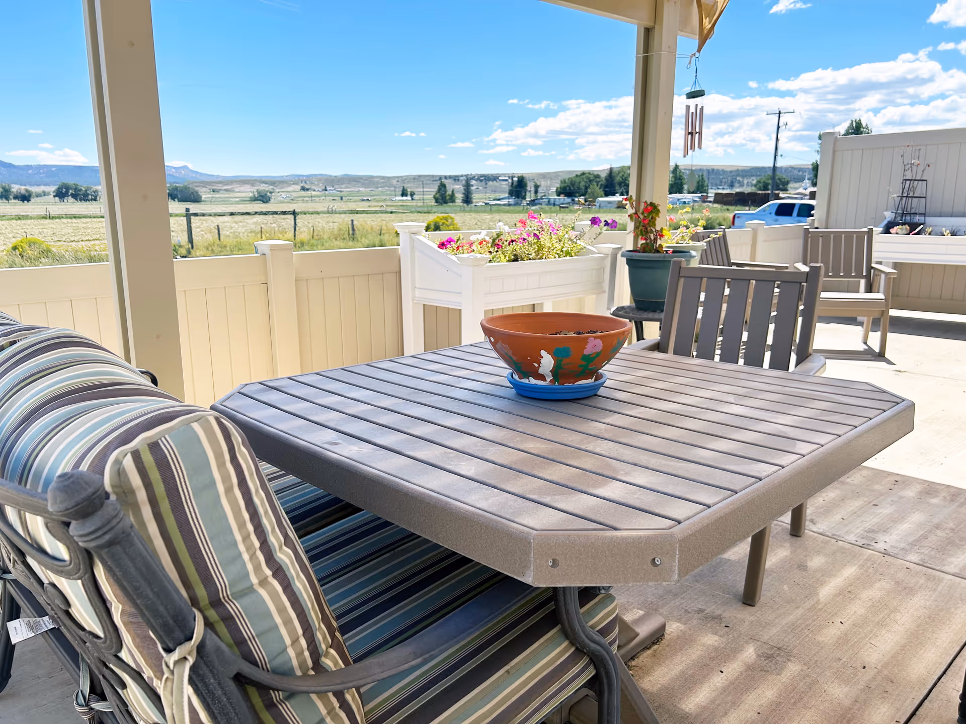 Outdoor patio with table, chairs, planters, and scenic countryside beyond a railing.