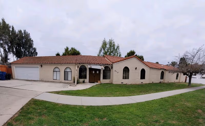 Front exterior of a single-story beige building with a red tile roof and curved driveway.