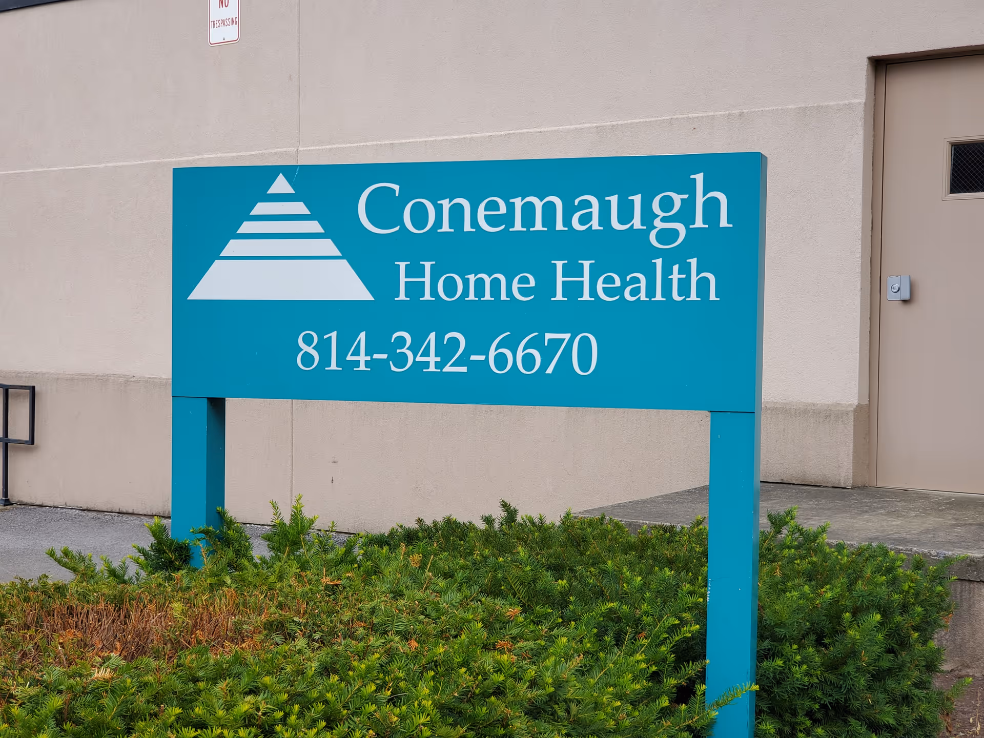 Outdoor teal sign for Conemaugh Home Health with logo and phone number near building