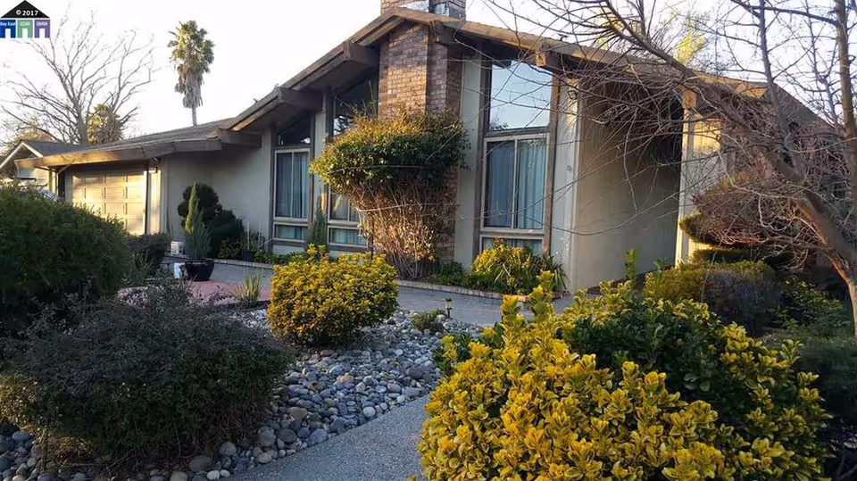 Front exterior of a single-story ranch-style house with a landscaped rock garden, shrubs, and a driveway.