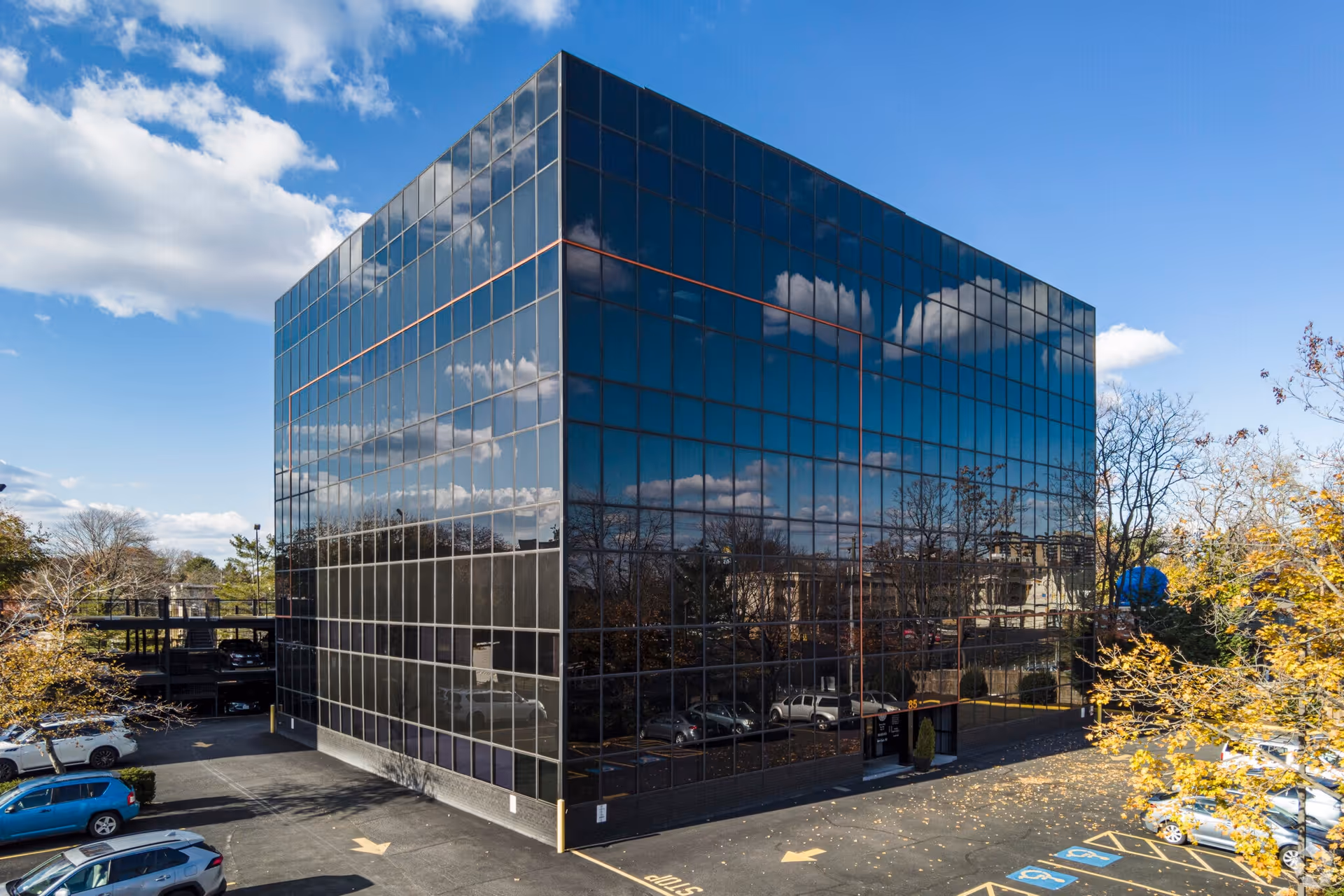 A modern glass-front building with a reflective facade and surrounding parking lot.