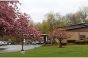 Exterior view of a brick senior living building with blossoming trees and a parking lot.