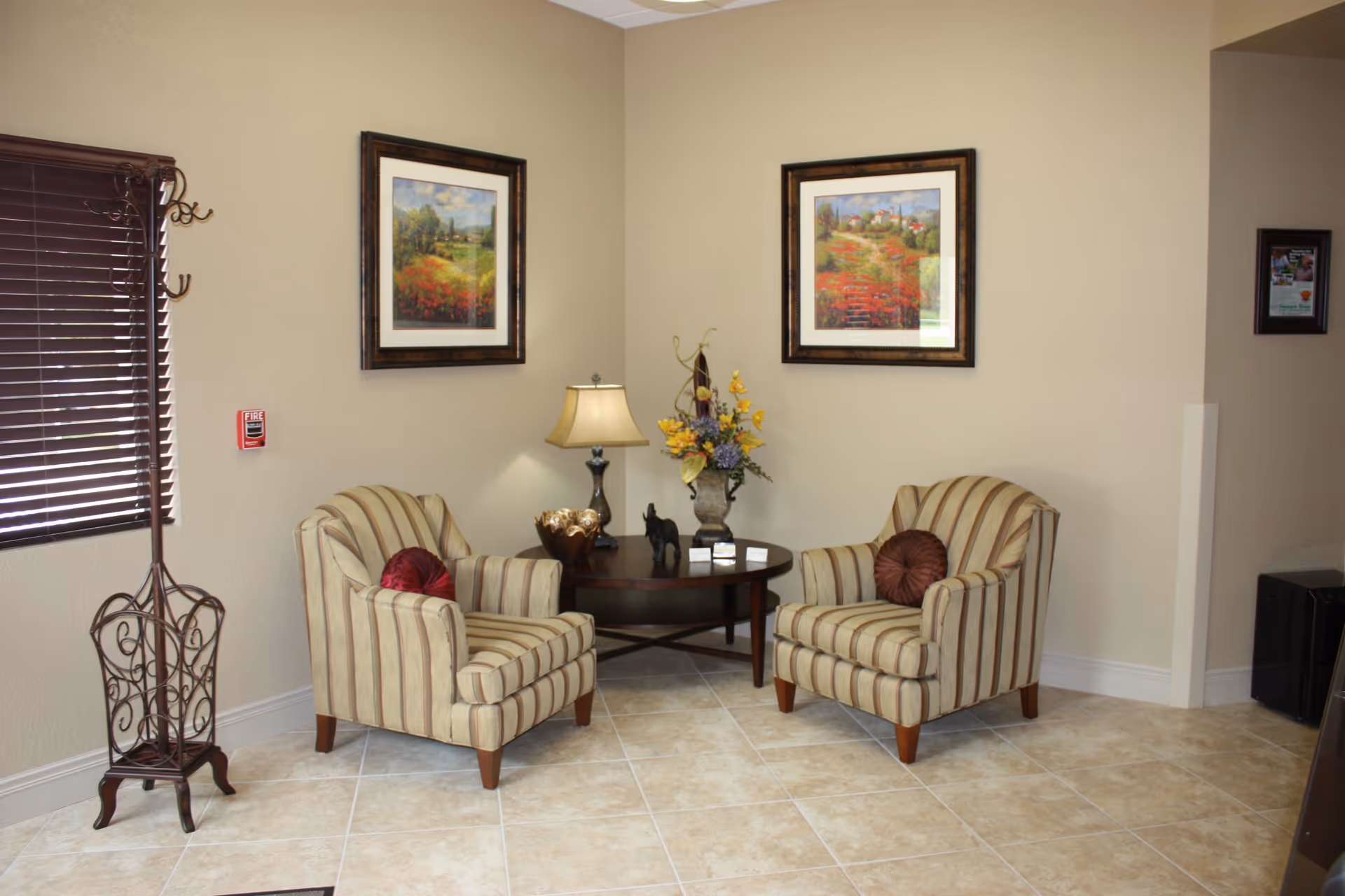 Two striped armchairs flank a round wooden table topped with a lamp and floral arrangement in a cozy beige seating area.