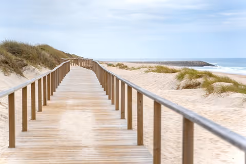 A wooden boardwalk extends through sandy dunes toward the ocean.