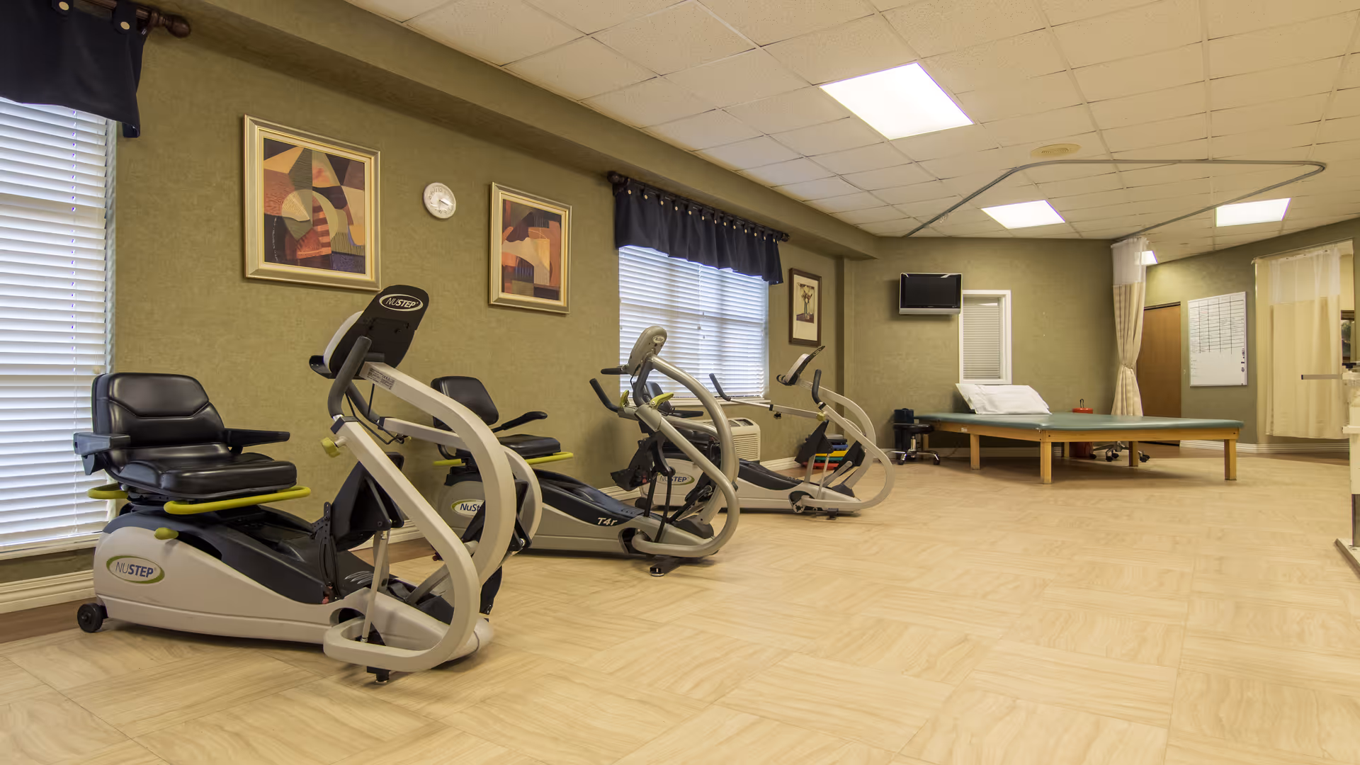 Interior view of a senior living gym with exercise machines and a therapy bed.