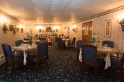 Dining room with tables set for meals and blue-upholstered chairs.