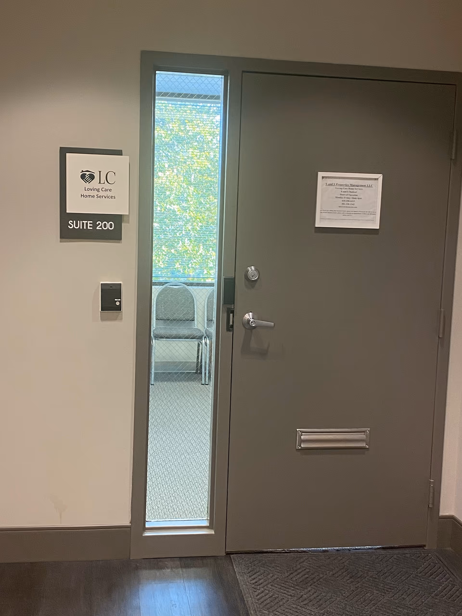 A gray metal door labeled Suite 200 adjacent to a glass panel with chairs visible beyond.