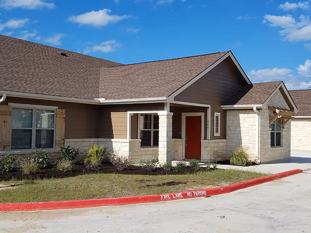 Front exterior of Emerald Cottages of Kerrville, a single-story facility with stone accents and red door.