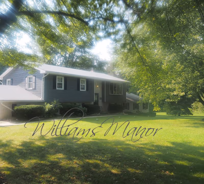 Exterior of a two-story gray building with Williams Manor sign on the lawn.