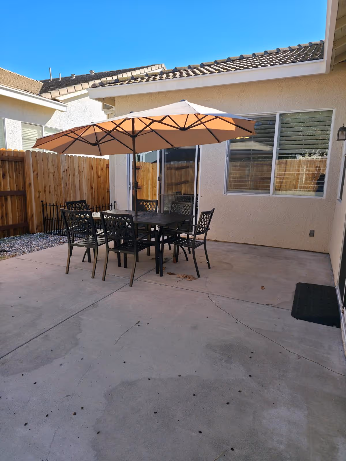 Patio area with a table, chairs, and umbrella beside a beige house.