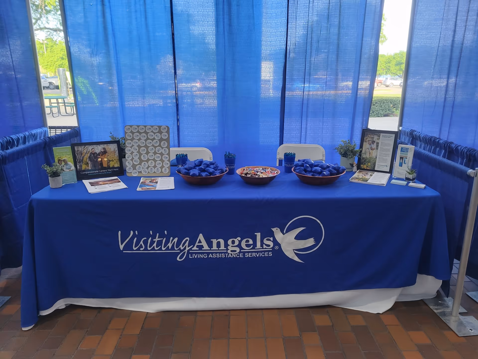 Indoor booth with a blue Visiting Angels tablecloth, brochures, and candy bowls.