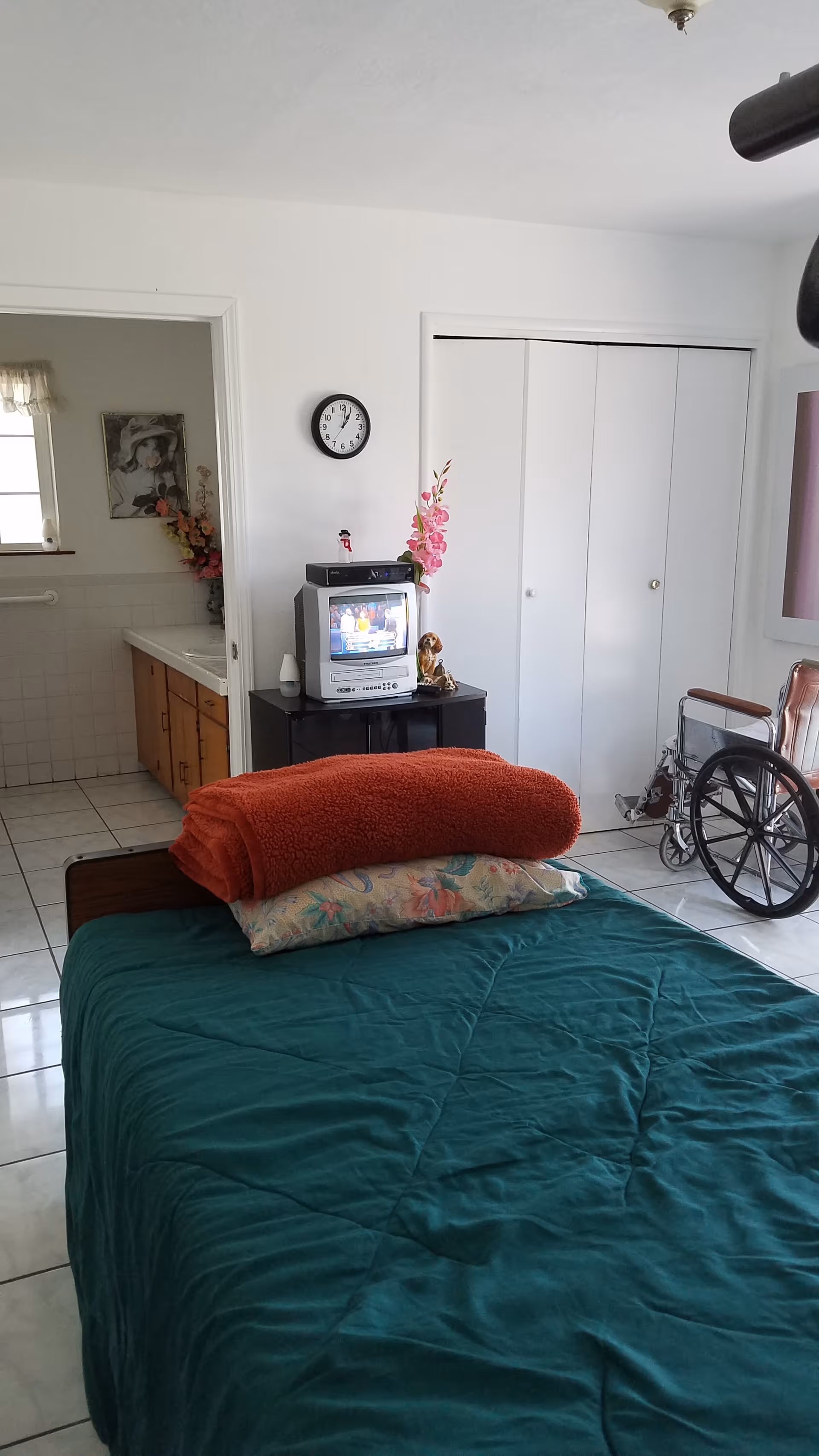 A bedroom at Hailey's Care Home with a bed, TV, wheelchair, and closet.