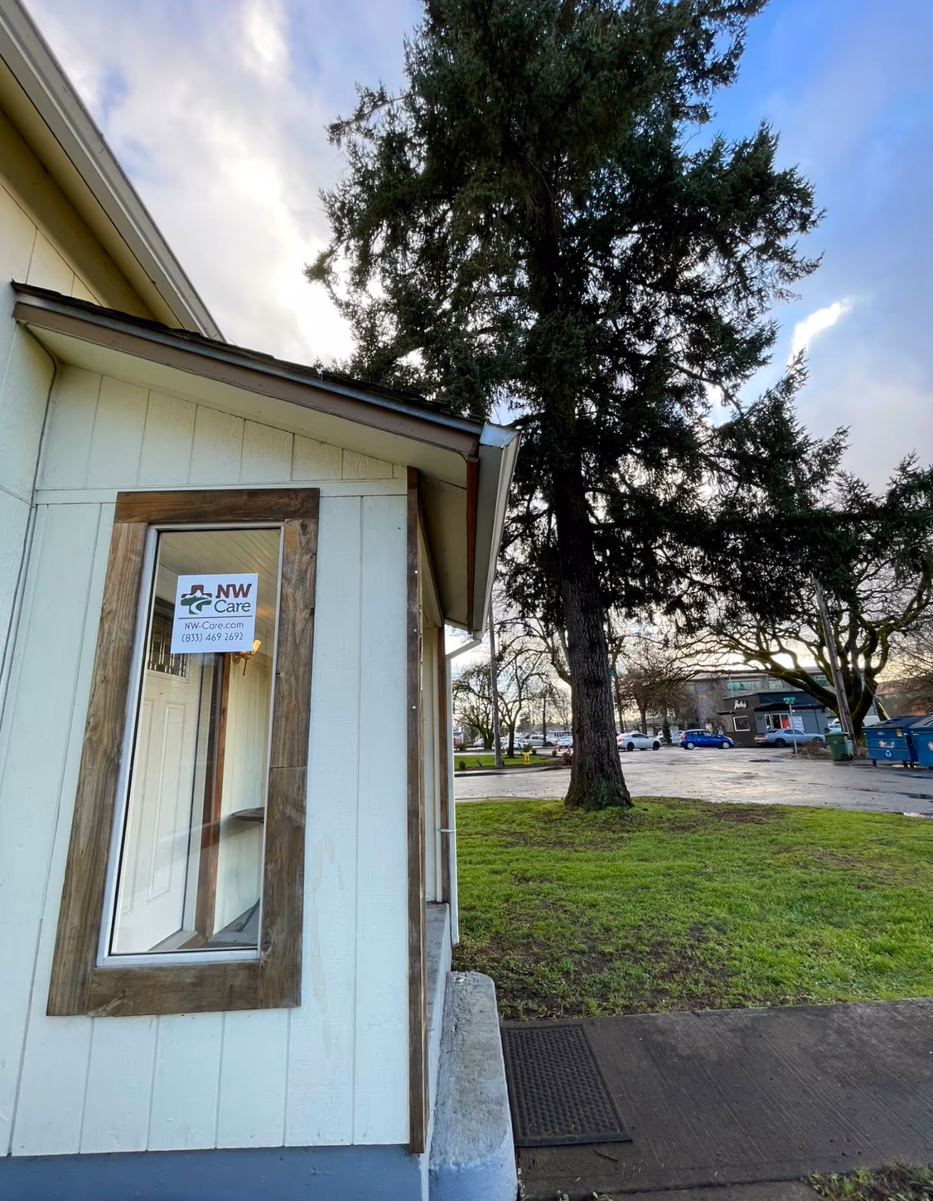The exterior of NWCare facility with a sign on the window, trees, and a parking lot.