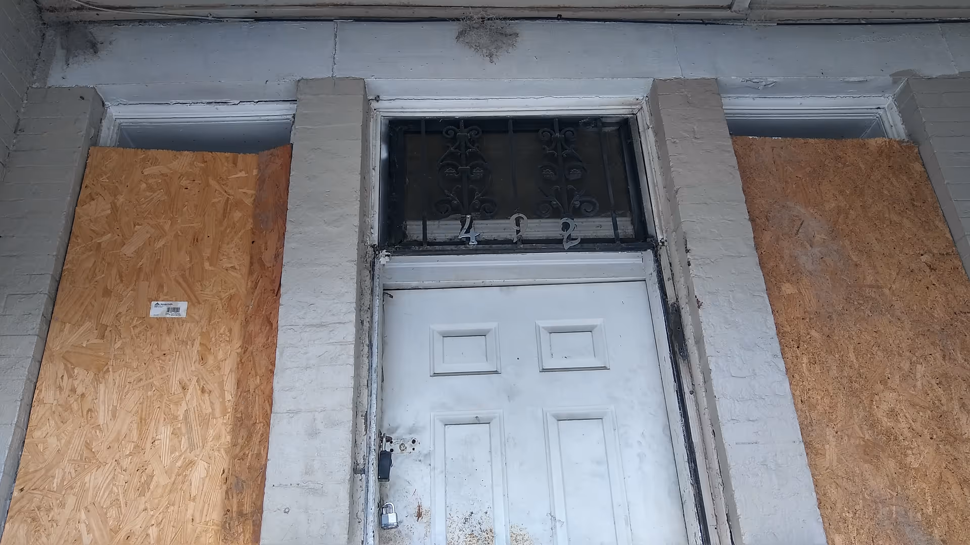 Boarded entrance to a building with a white door and plywood coverings on the sides.