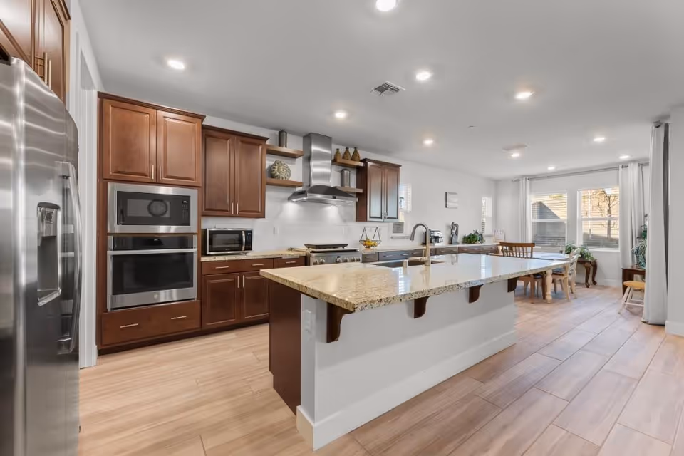 Modern kitchen with island, stainless appliances, wooden cabinets, and adjoining dining area.