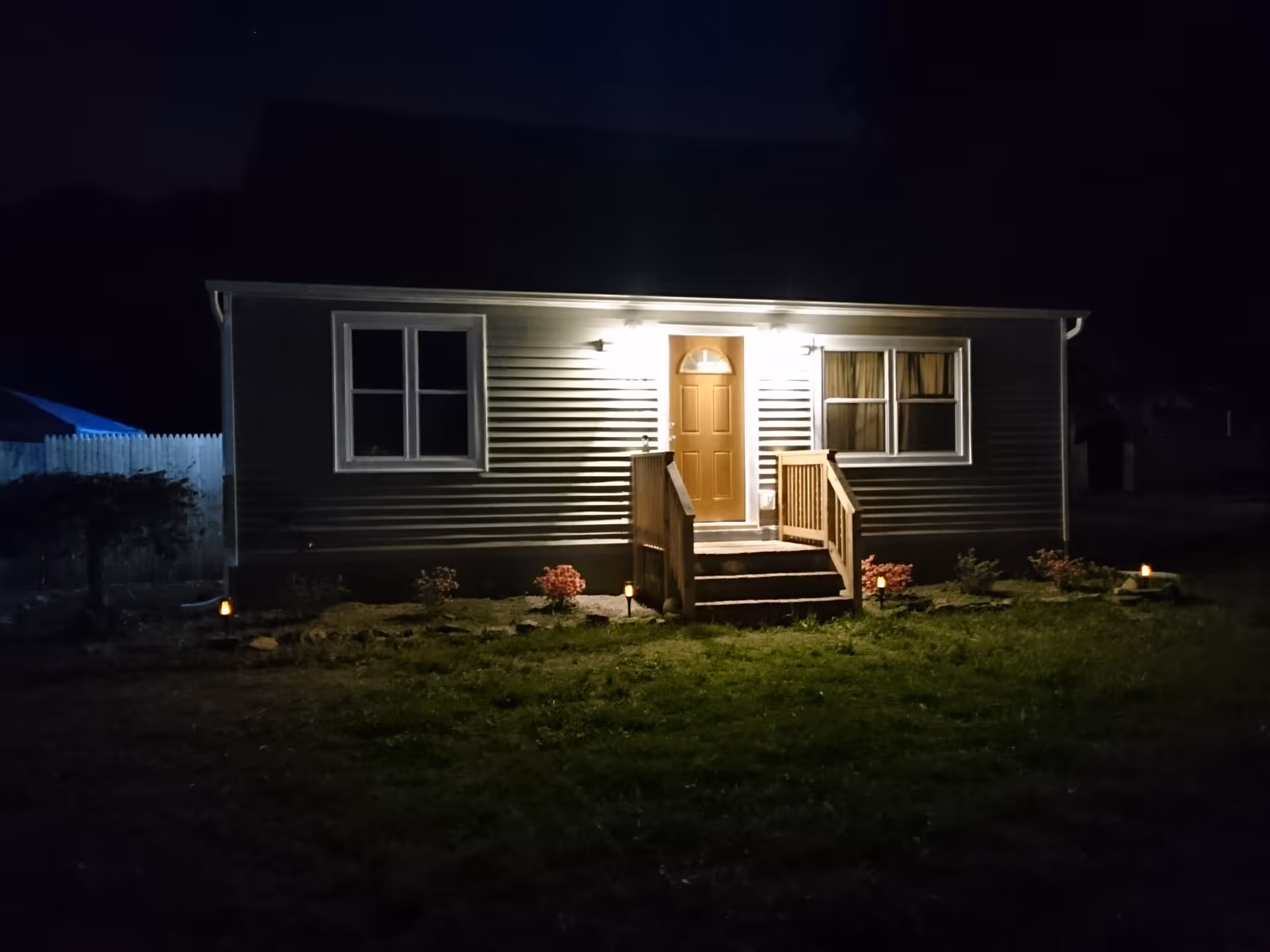 Nighttime exterior of a single-story facility with a lit front door and small garden.