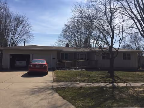 Single-story building exterior with a driveway, red car, and leafless trees in front.