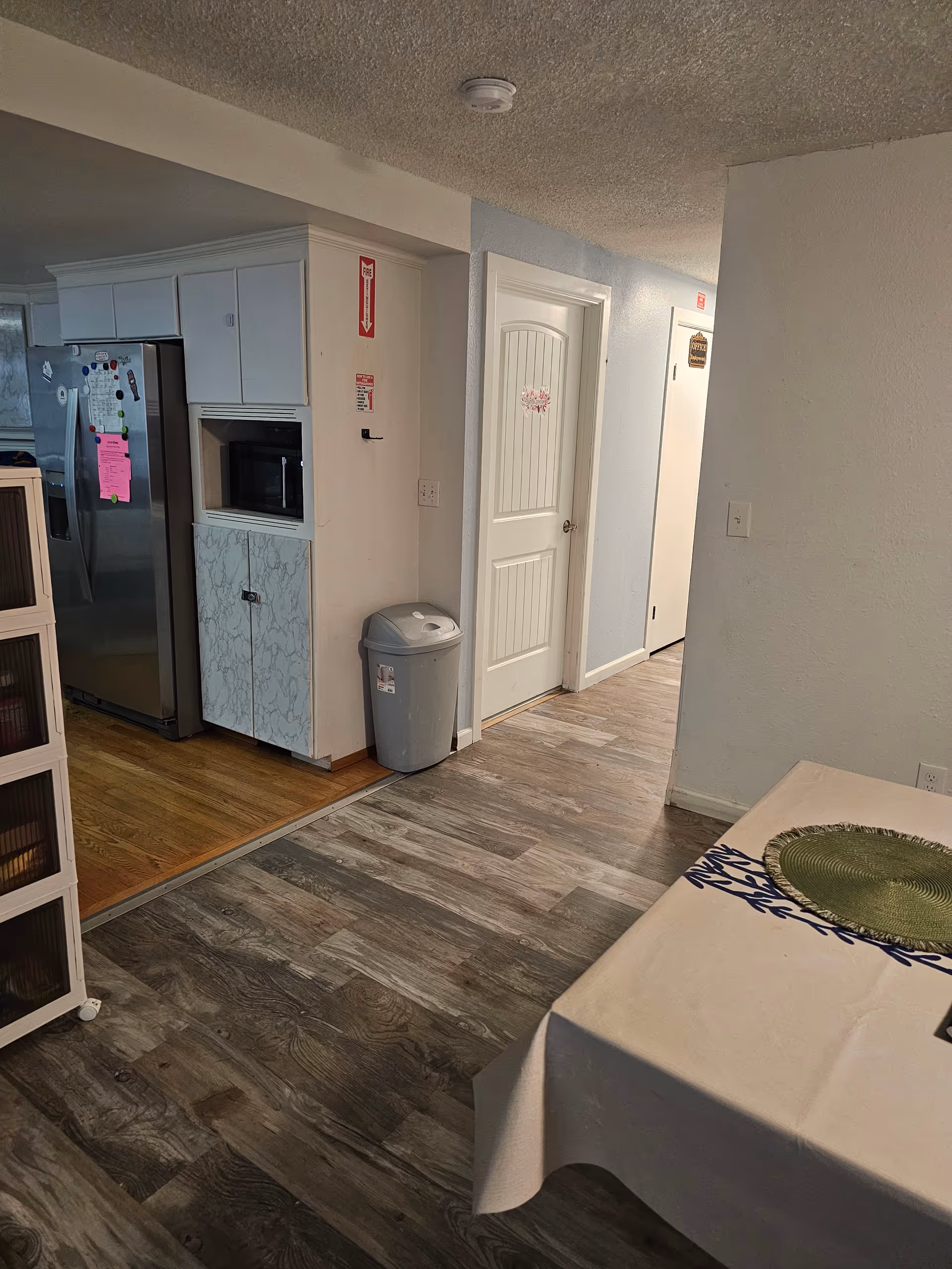 Kitchen area with fridge, microwave, cabinets, trash can, and dining table.