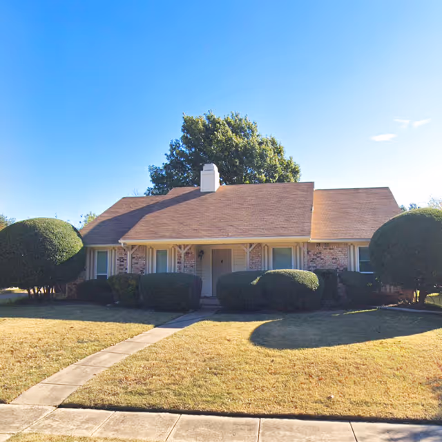 Front exterior of a single-story brick building with trimmed hedges and a sidewalk.