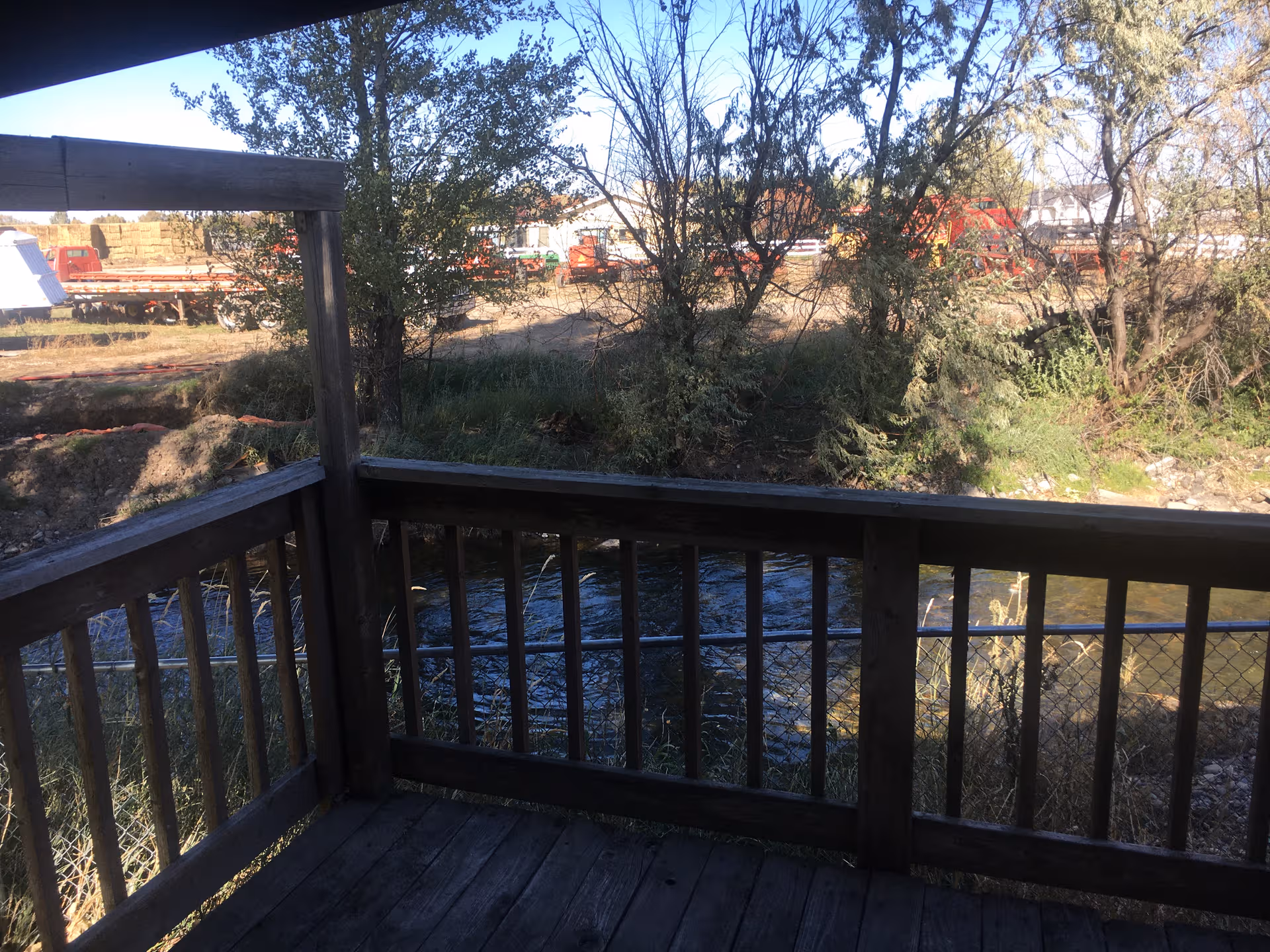 Wooden deck overlooking a river with trees and distant construction equipment.