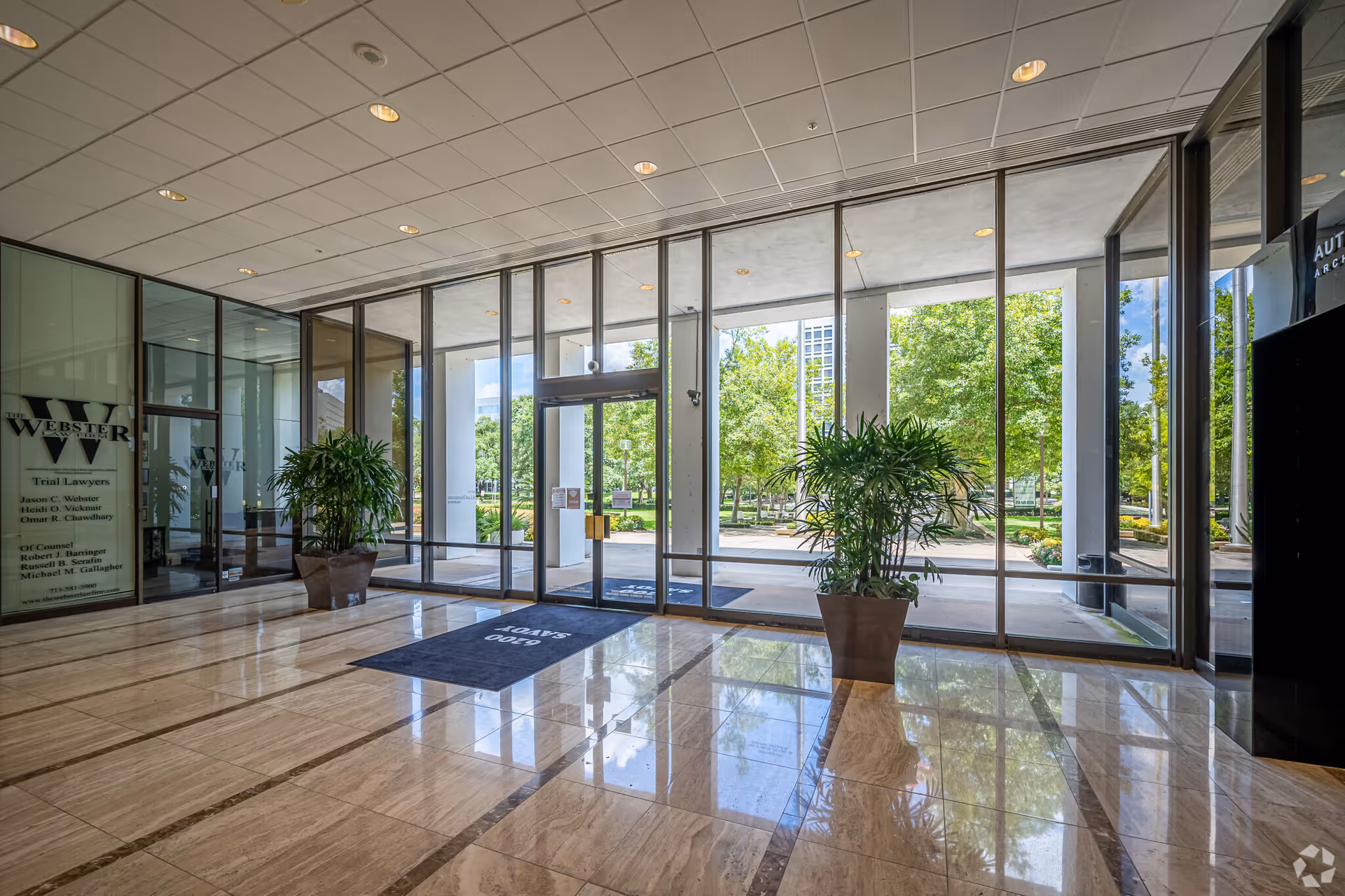 Bright lobby with glass doors, marble floor, and large potted plants.