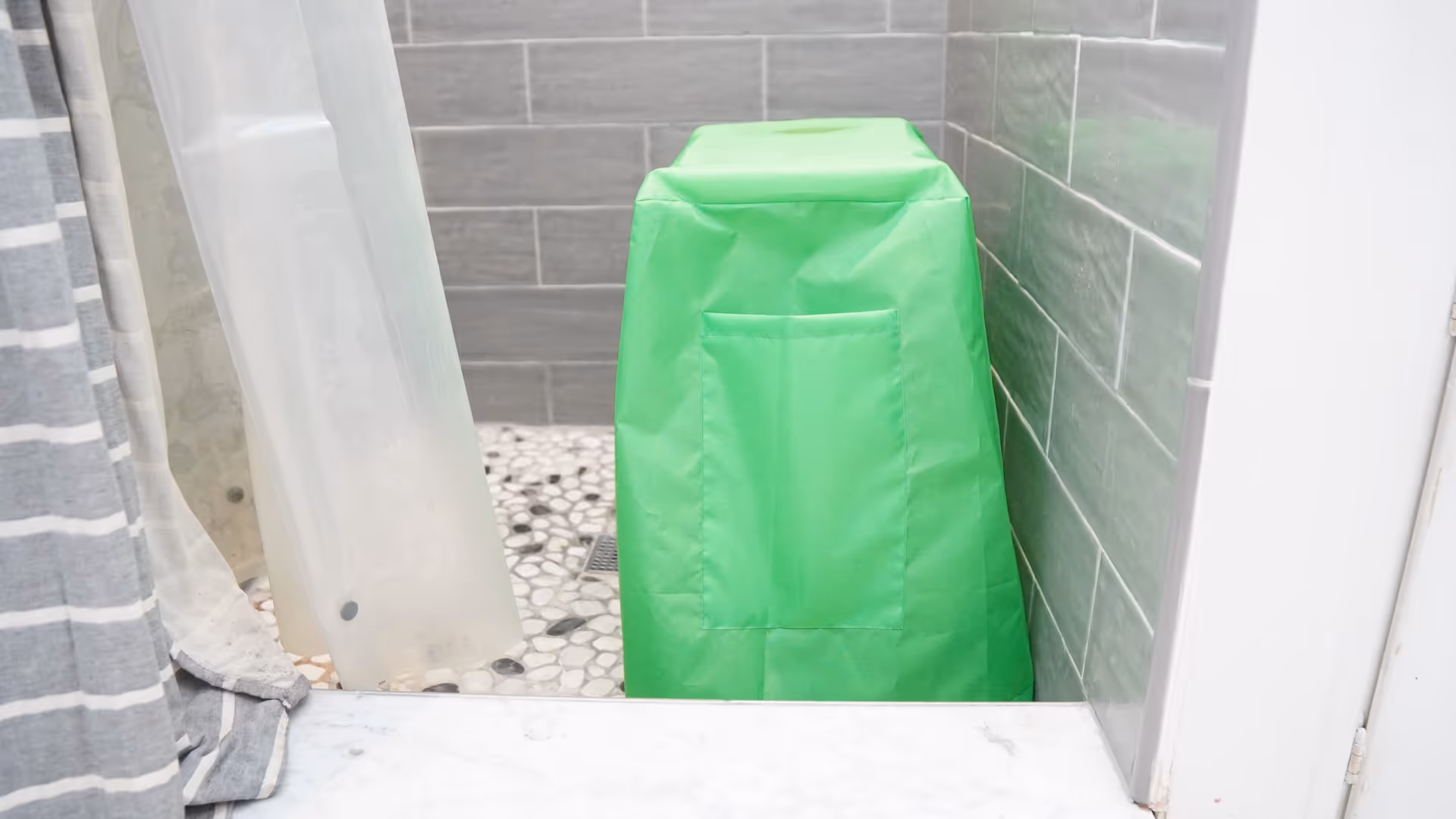 Green wrapped object in a tiled bathroom shower with a curtain.