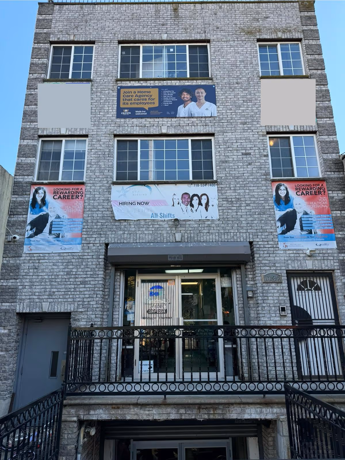 Brick-front building with multiple banners advertising Crown Home Care and employment; glass entrance in center.
