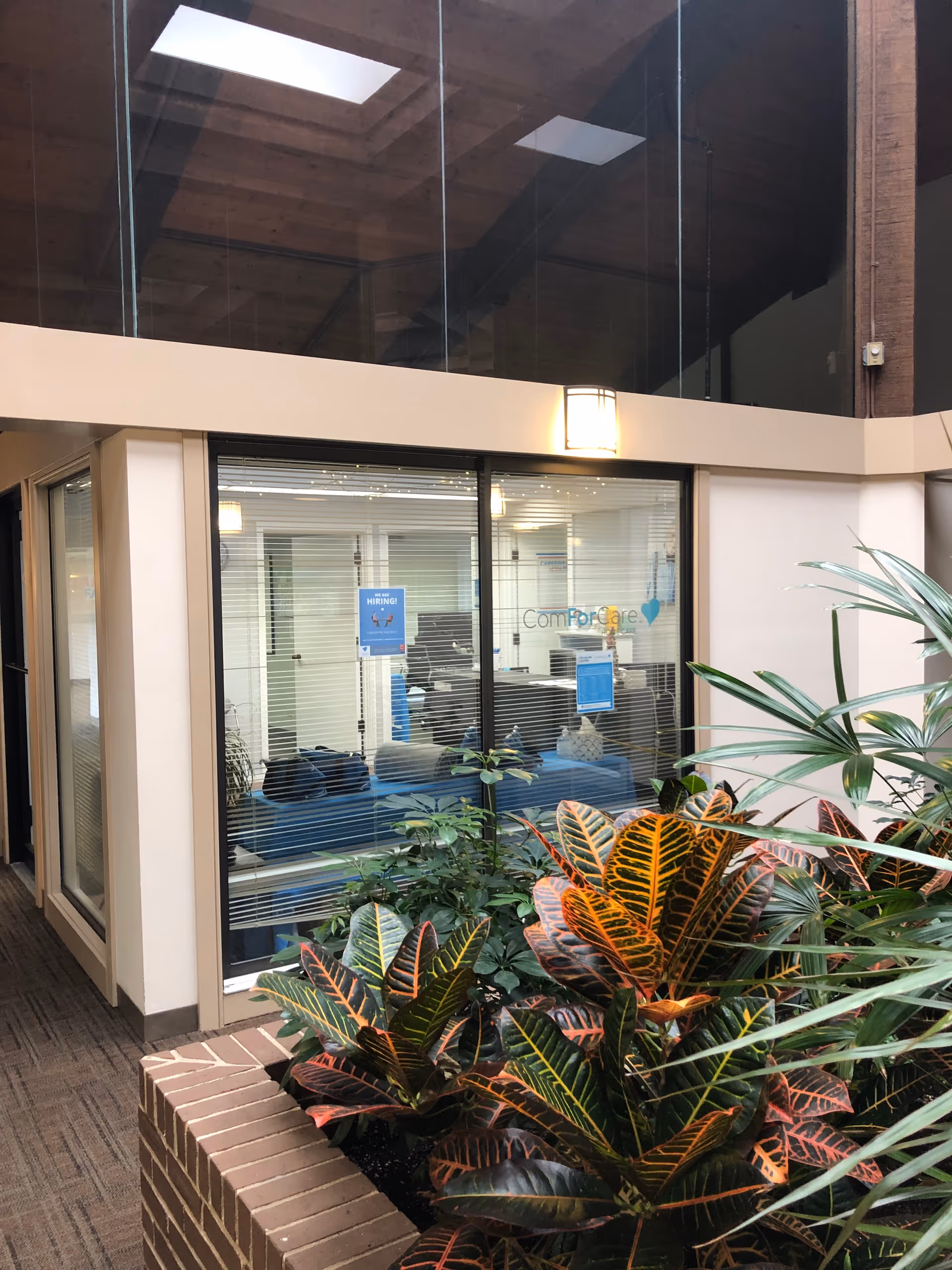 Indoor lobby with glass-walled office labeled ComForCare and tropical plants.