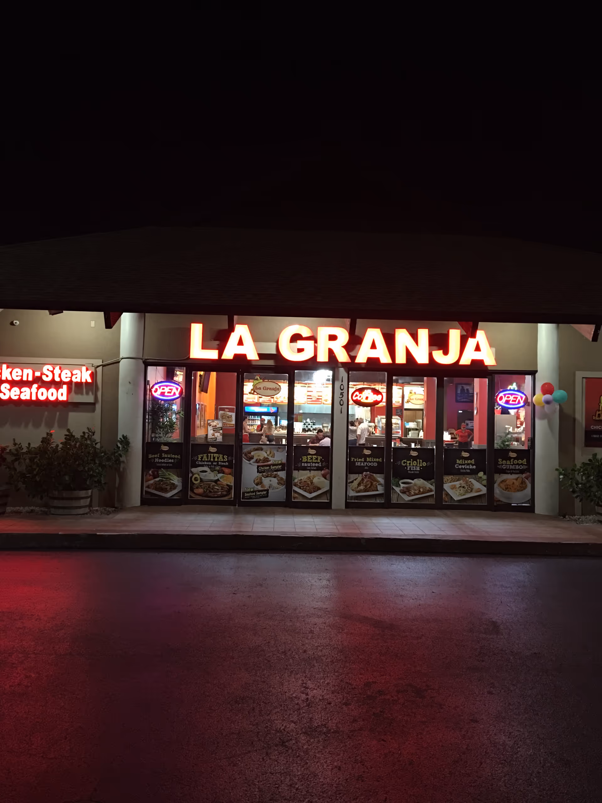 Nighttime storefront of La Granja restaurant with illuminated sign and diners inside.