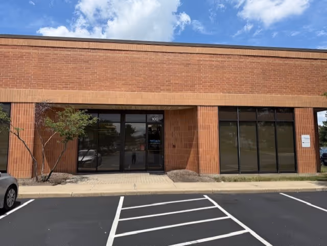 Brick building with glass doors and a parking lot in the foreground.