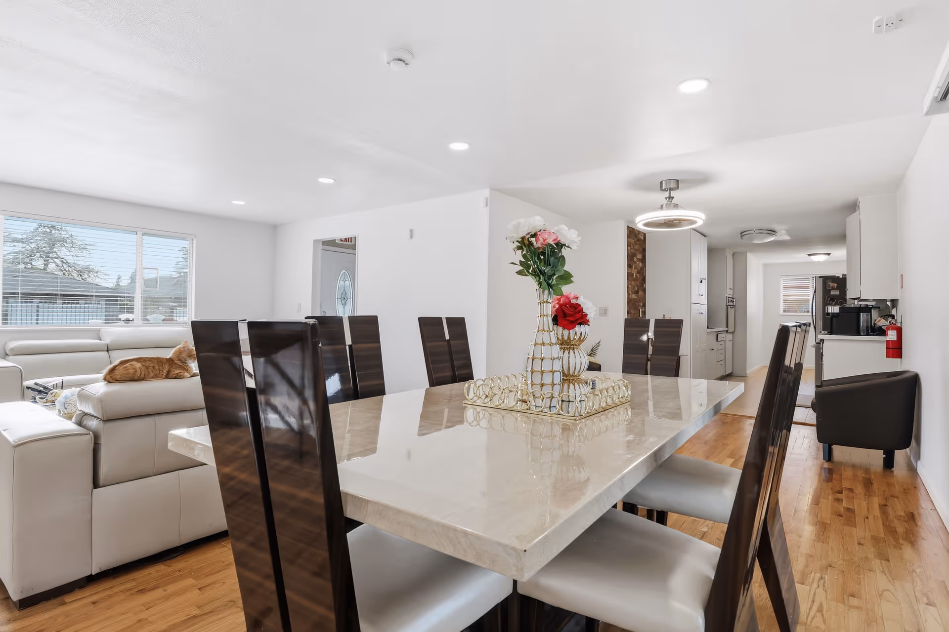 Bright dining room with a large marble table, dark chairs, and a living area visible.