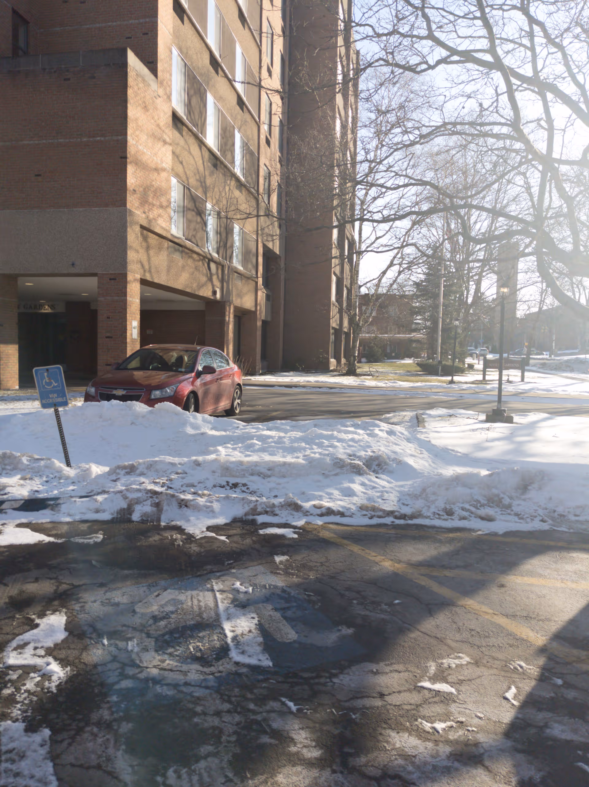 Exterior view of Wesley Gardens facility with snow-covered parking, a red car, and leafless trees.