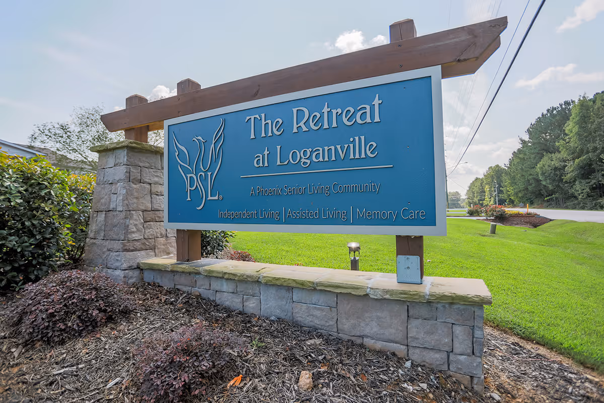 Blue sign reading The Retreat at Loganville on a stone base beside manicured lawn.