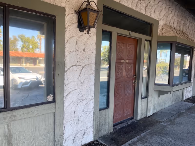 Exterior view of a building entrance with a brown decorative door and surrounding windows.