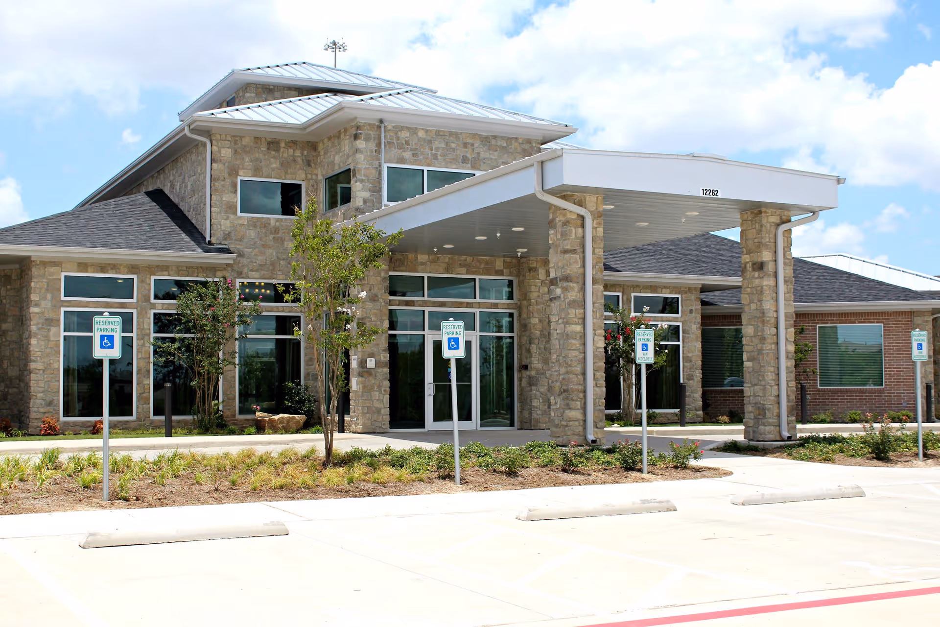 Stone-faced senior living facility entrance with glass doors and a covered porte-cochère.