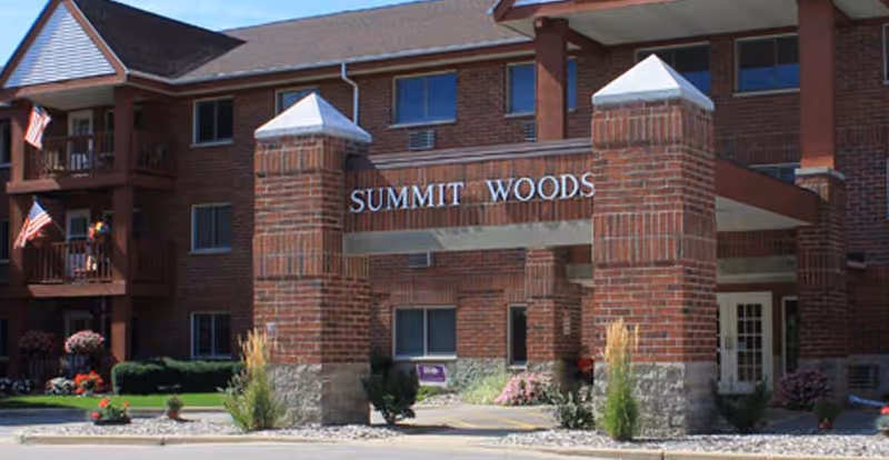 Exterior view of Summit Woods senior living entrance with brick pillars and landscaping.