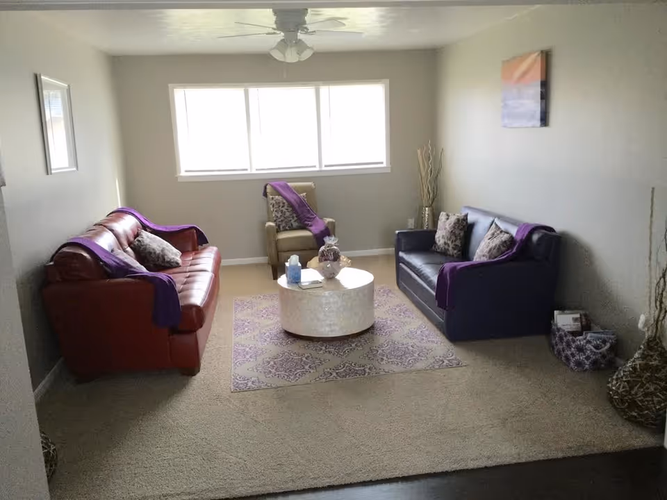 Cozy living room with red and purple couches, coffee table, and sunlit window.