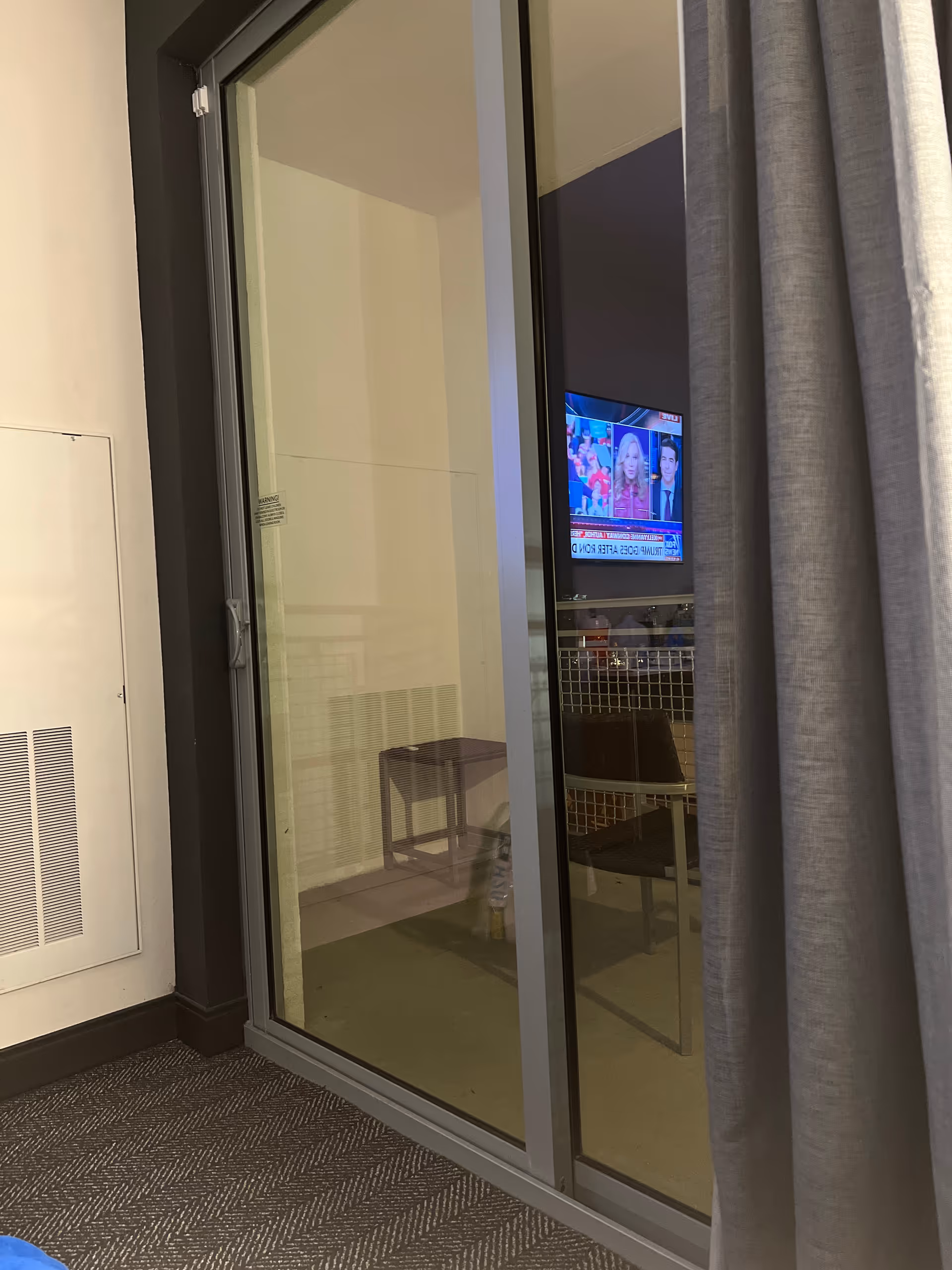 Interior room with sliding glass door, TV on wall, and small furniture beside curtain.