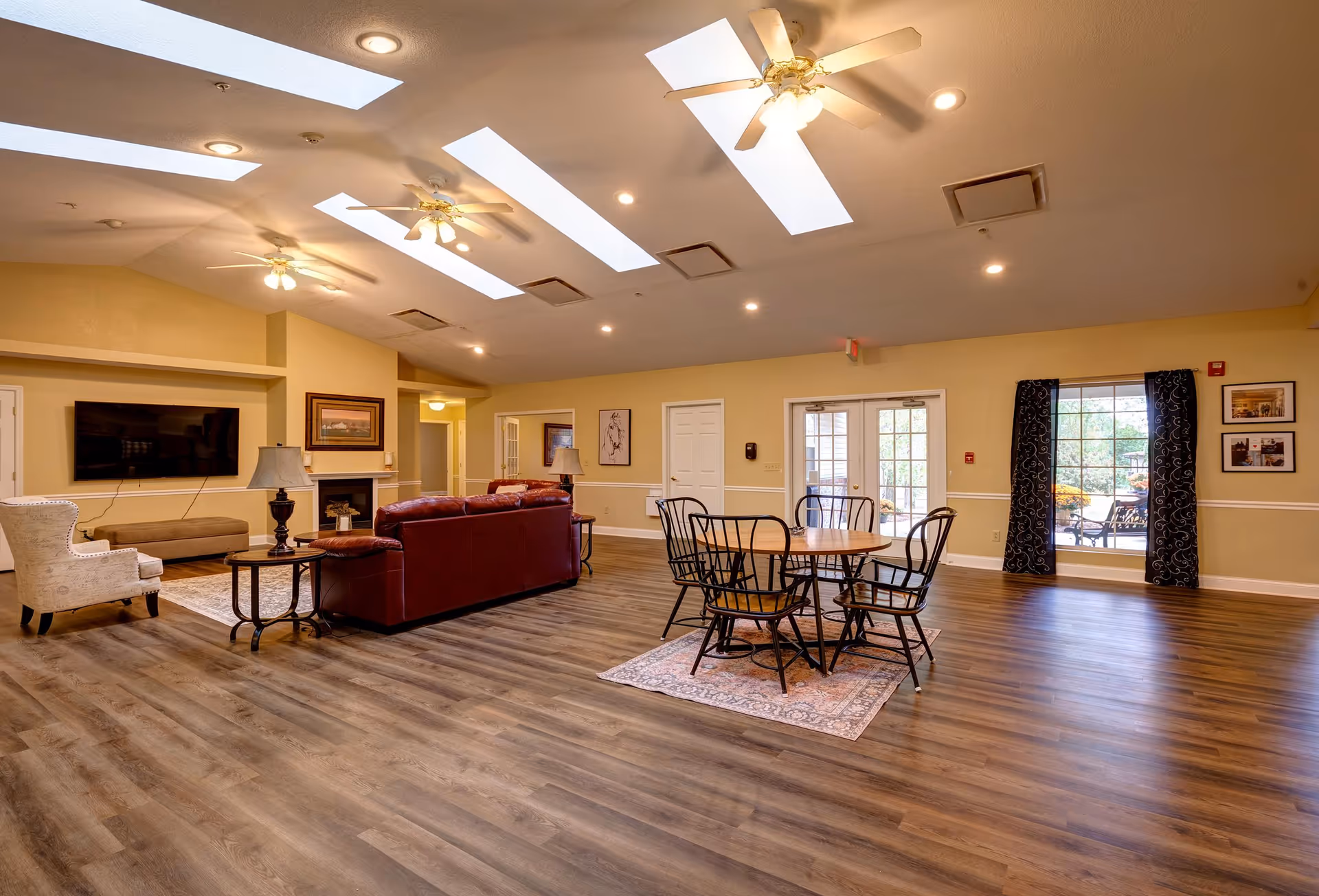 Spacious senior living lounge with a red leather sofa, dining table, and skylight ceiling.