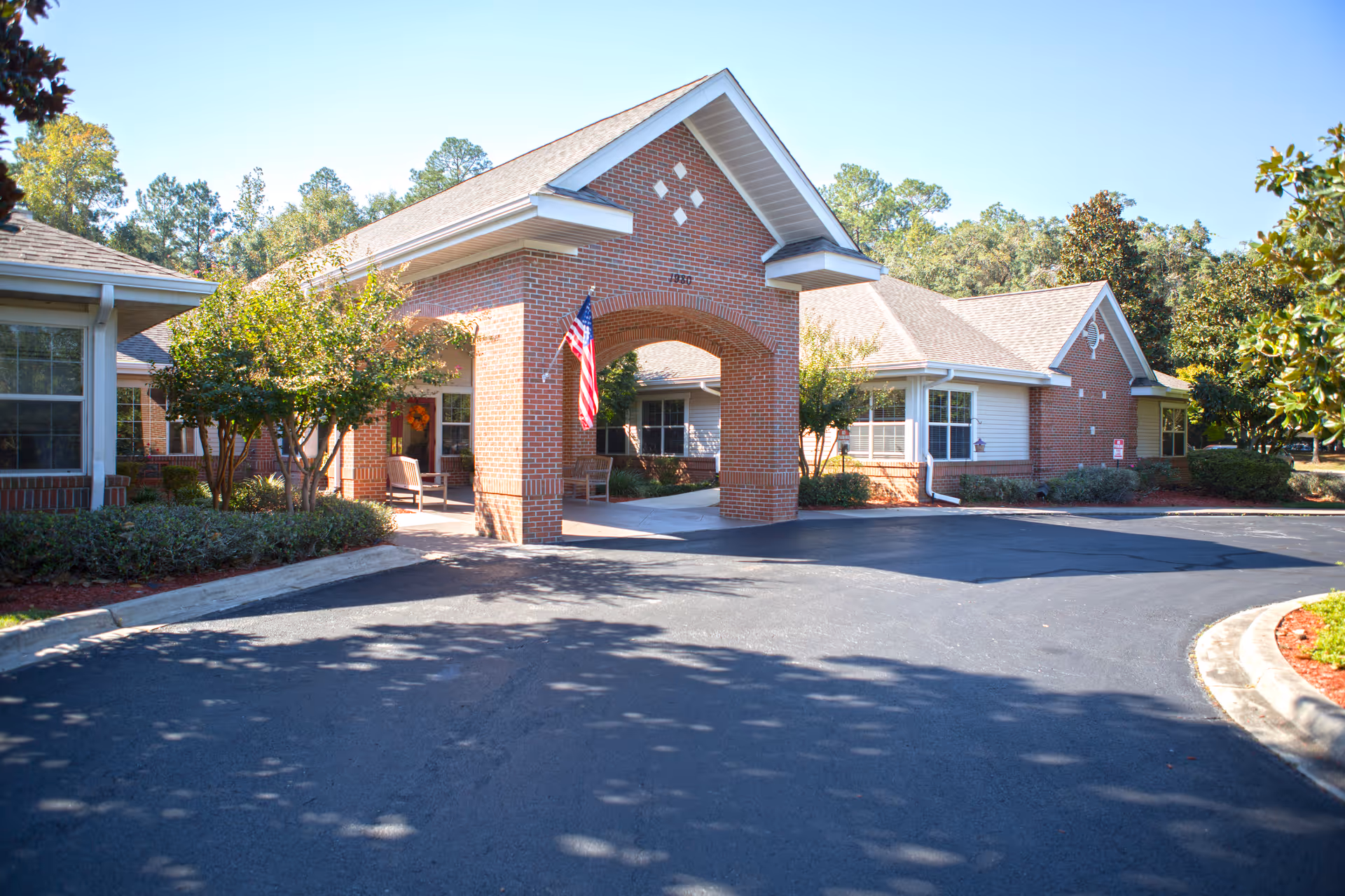 Brick senior living facility entrance under a curved arch with American flag and driveway