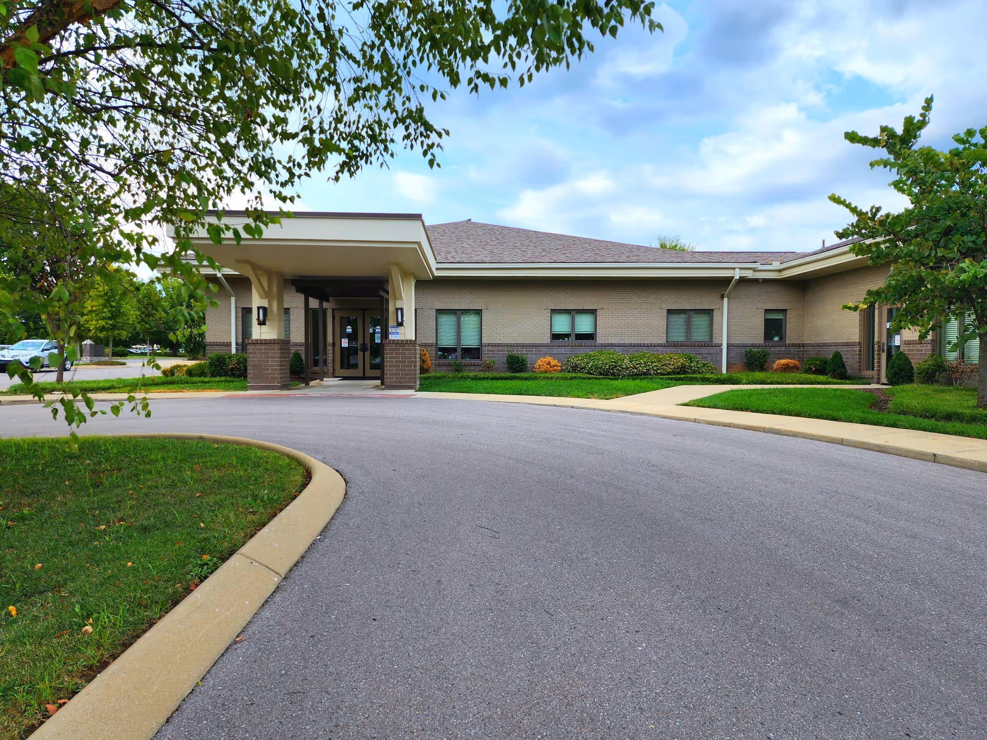 Brick hospice facility exterior with covered entrance, curved driveway, and landscaped grounds.
